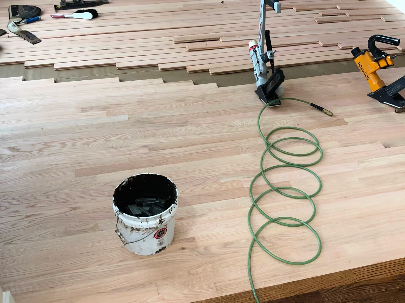 Unfinished oak boards going down, flooring nailer and air hose on the floor
