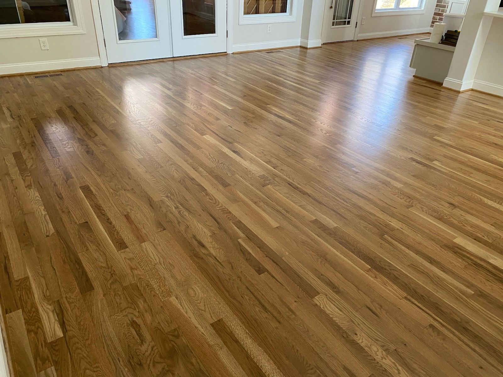 Refinished hardwood in a natural tone running through French doors into the next room