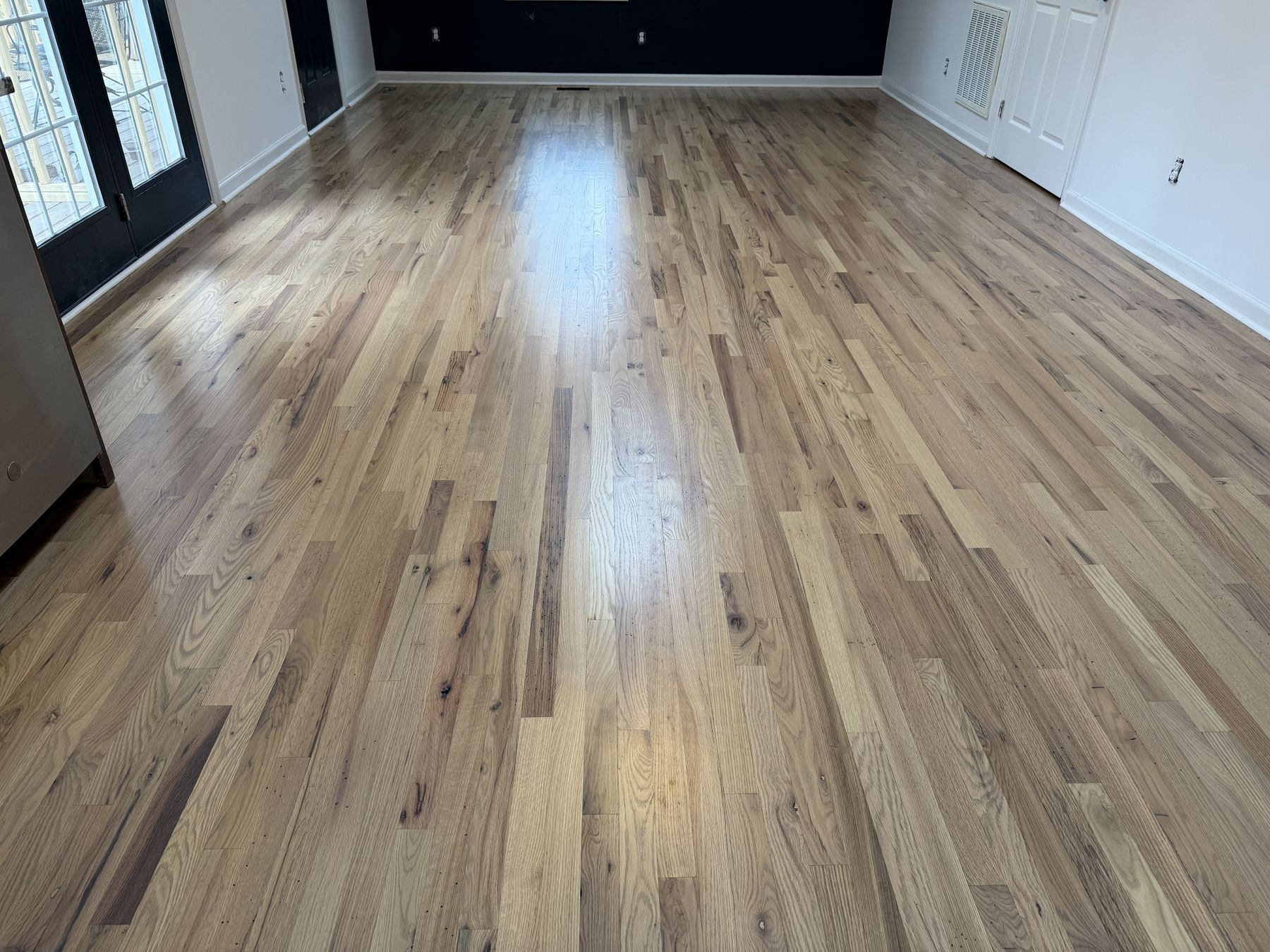Refinished hardwood in a natural tone, dark accent wall at the far end